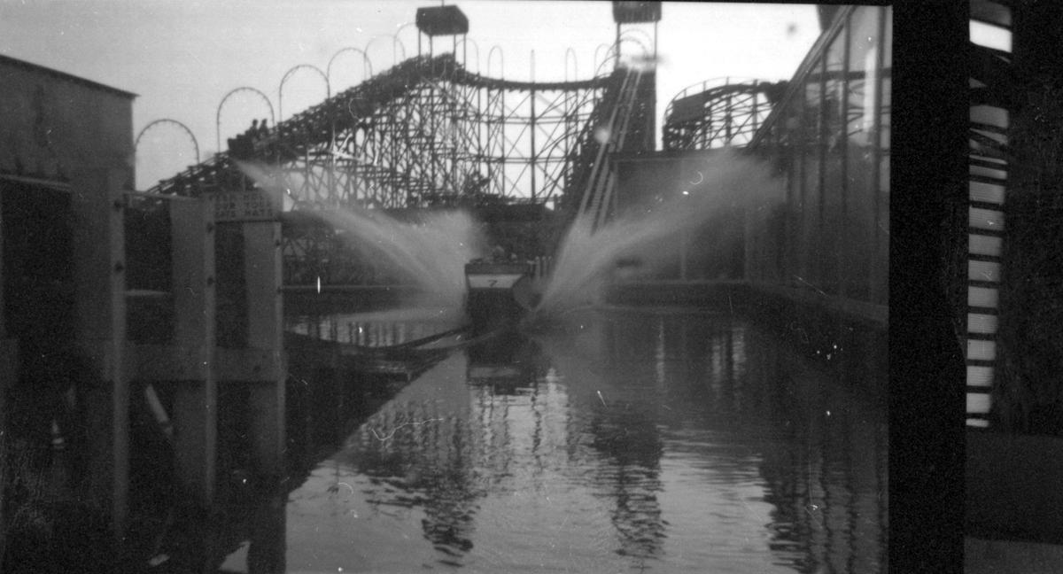 Black and white photograph of a water splash fairground ride, just as the car hits the water.