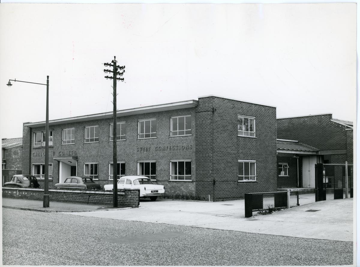 Black and white photograph of a two-storey modernist light industrial block with the name SWEET CONFECTIONS on the front.