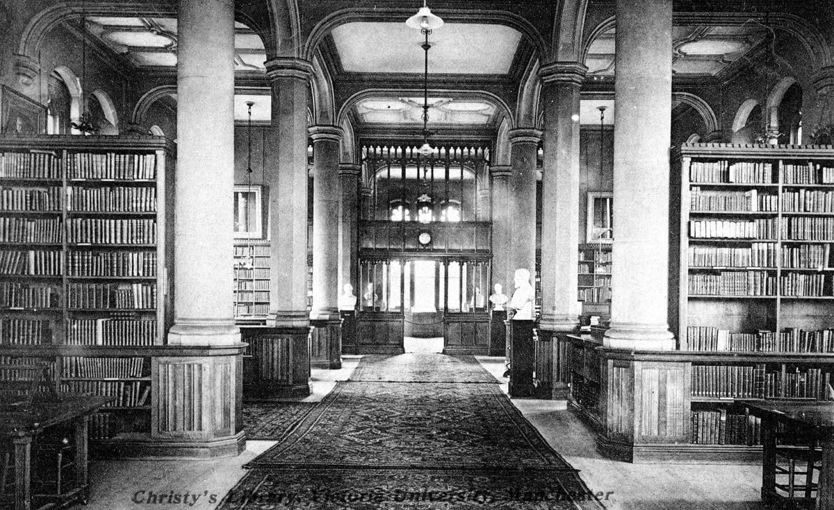 Black and white photograph of the interior of a library with large pillars and dark wood shelves full of books.